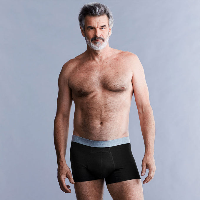 Mann trägt schwarze, waschbare und schützende TENA Men Inkontinenz-Boxershorts vor neutralem grauen Hintergrund.